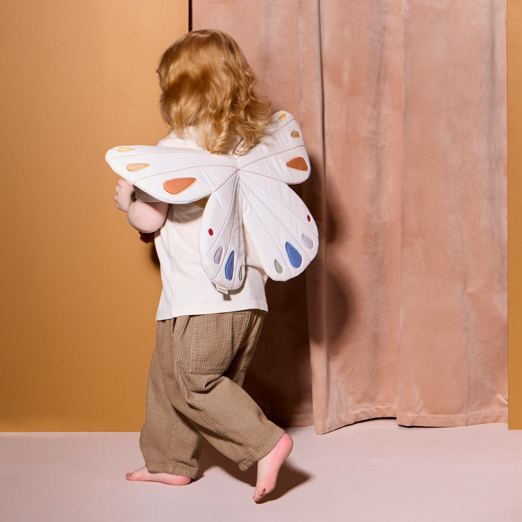 Quilted white butterfly-shaped costume with pastel orange, blue, and purple accents on wings. Features tan straps, creating a playful, whimsical tone.
