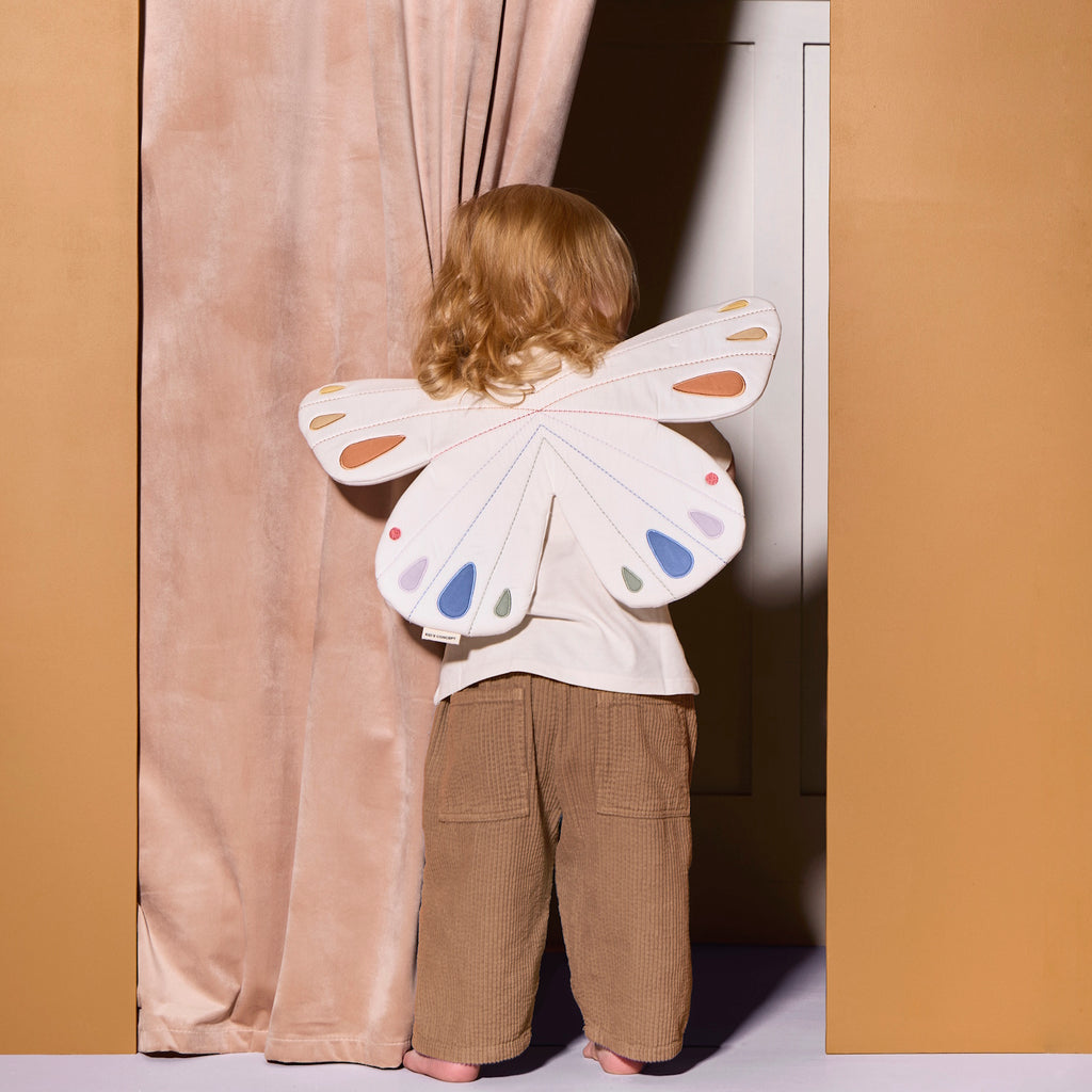 Quilted white butterfly-shaped costume with pastel orange, blue, and purple accents on wings. Features tan straps, creating a playful, whimsical tone.