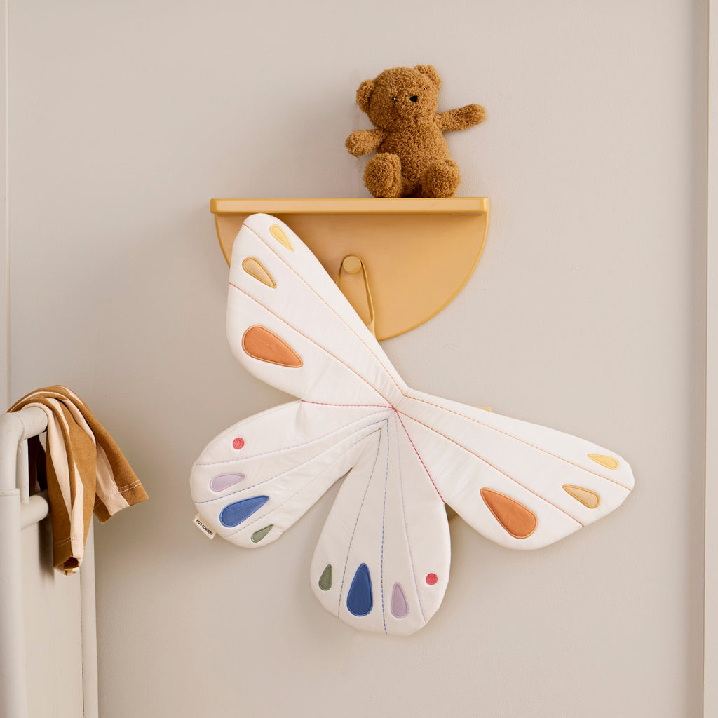 Quilted white butterfly-shaped costume with pastel orange, blue, and purple accents on wings. Features tan straps, creating a playful, whimsical tone.