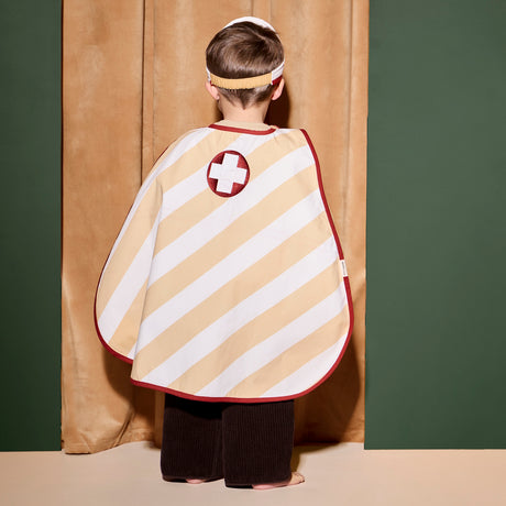 Back view of a child wearing a striped doctor dress-up cape with a medical cross emblem.