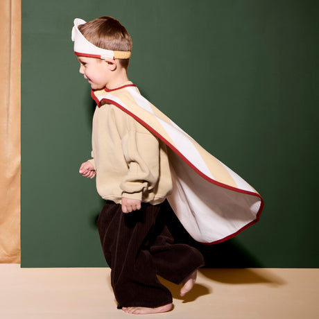 Child wearing a doctor headband and cape running in profile against a green backdrop.