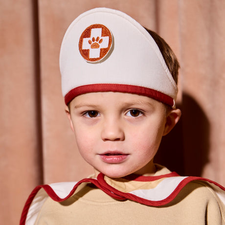 Young child wearing a white and red vet costume hat with a paw print badge.