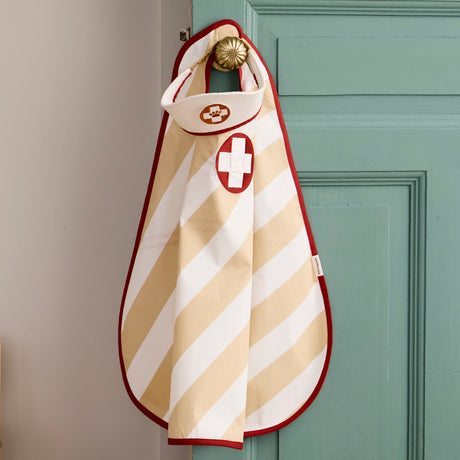 Kids doctor apron and hat costume set hanging on a brass knob of a green wooden door.