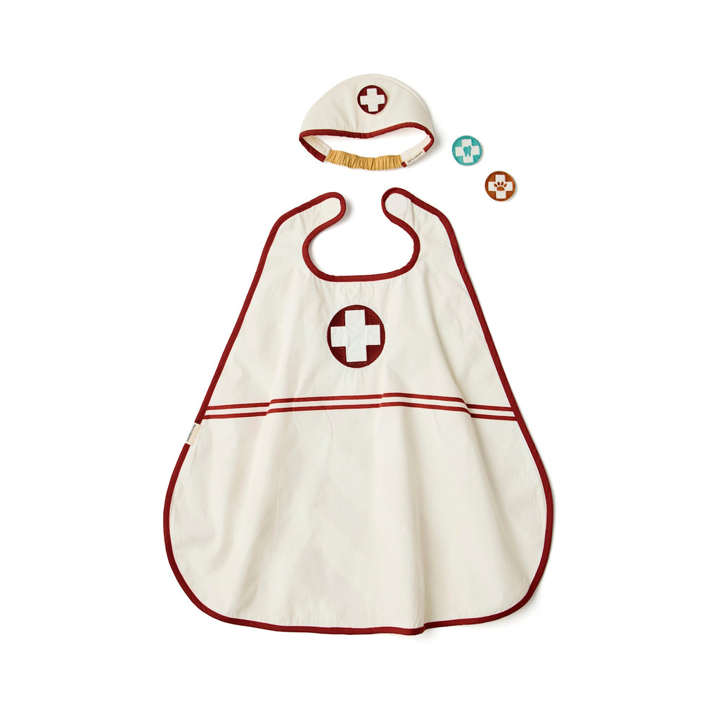 A child's doctor costume set includes a white apron and cap, both with red cross symbols, along with two round fabric badges. The tone is playful and imaginative.