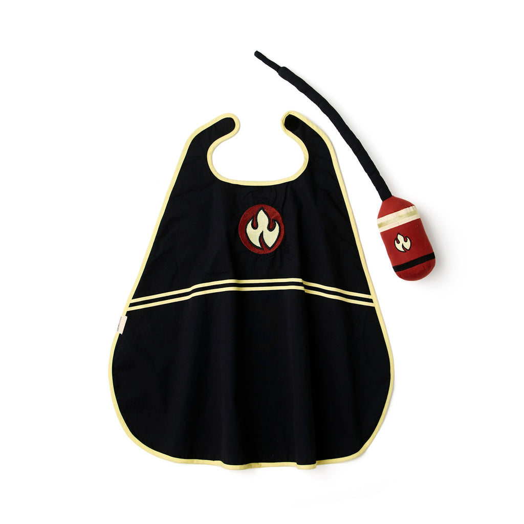 Black children's cape with yellow trim and a red flame emblem. Accompanied by a matching red plush toy with a yellow stripe and flame design. Playful tone.