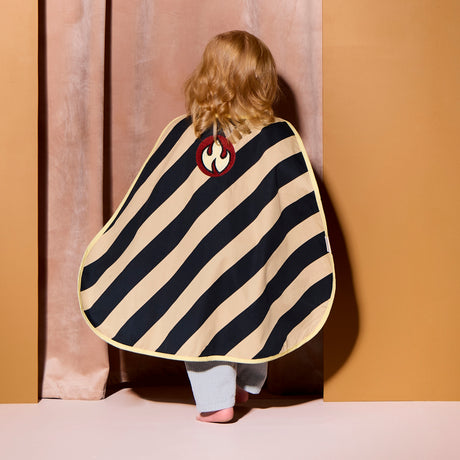 Back view of a child wearing a black and tan striped dress-up cape with a flame emblem patch.