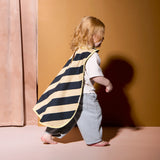 Toddler with blonde curly hair walking in profile while wearing a striped dress-up cape and gray trousers.