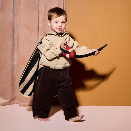 Young child wearing a firefighter cape dress-up set and playing with a fabric hose prop.