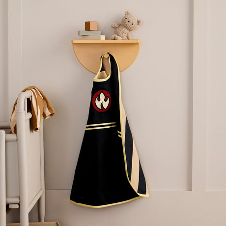 A black firefighter cape hanging from a wall hook under a shelf with toys in a children's room.