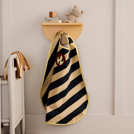 Striped firefighter dress-up cape with flame emblem hanging on a wall shelf peg in a kid's room.