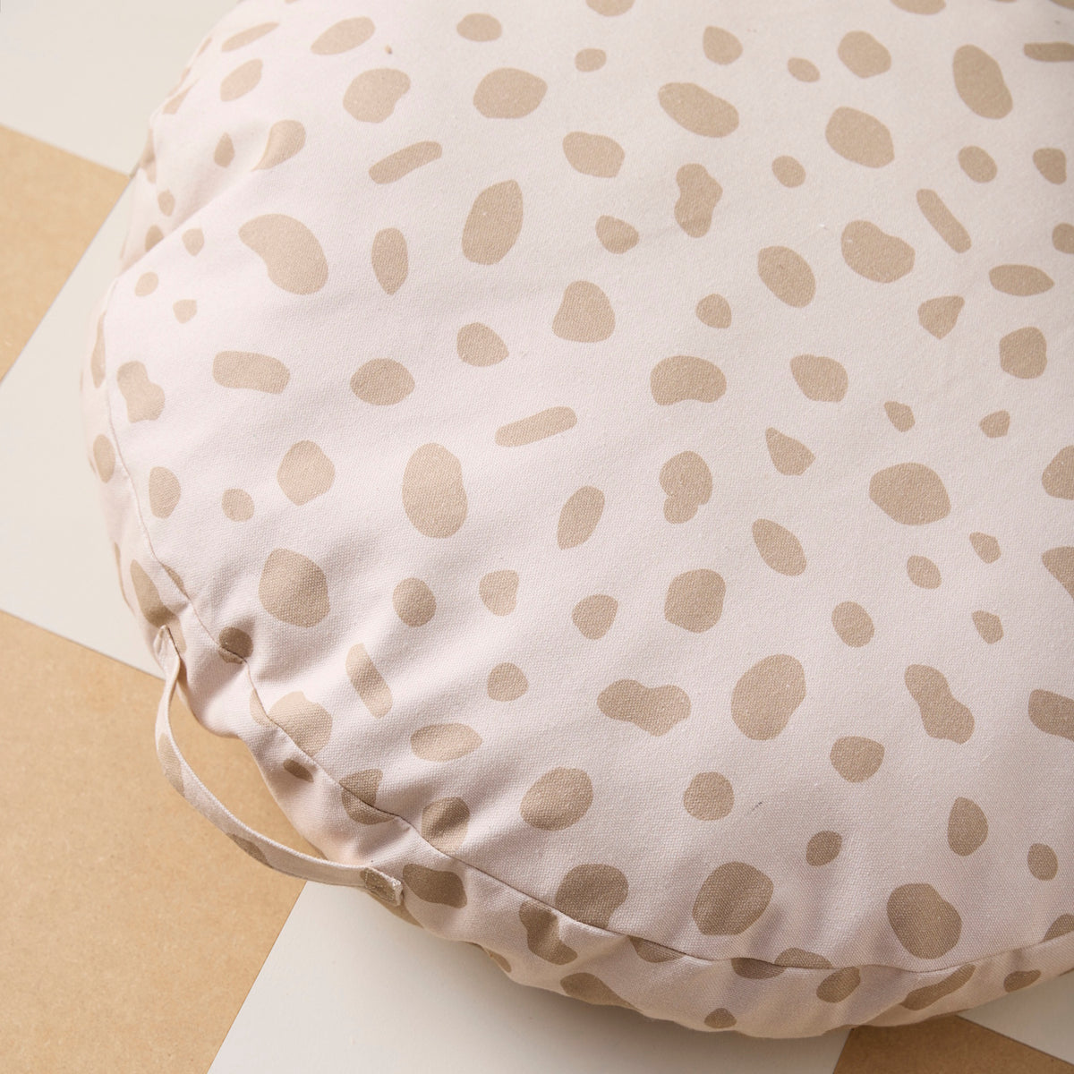 Close-up of a round, beige spotted floor cushion with a fabric carrying handle.