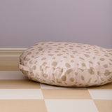 A round, beige polka-dot floor cushion resting on tiled flooring against a plain wall.