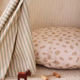 Round spotted floor cushion inside a play tent beside small wooden toys.