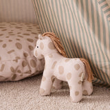 Spotted plush horse toy standing on a rug next to a matching cushion and striped fabric.