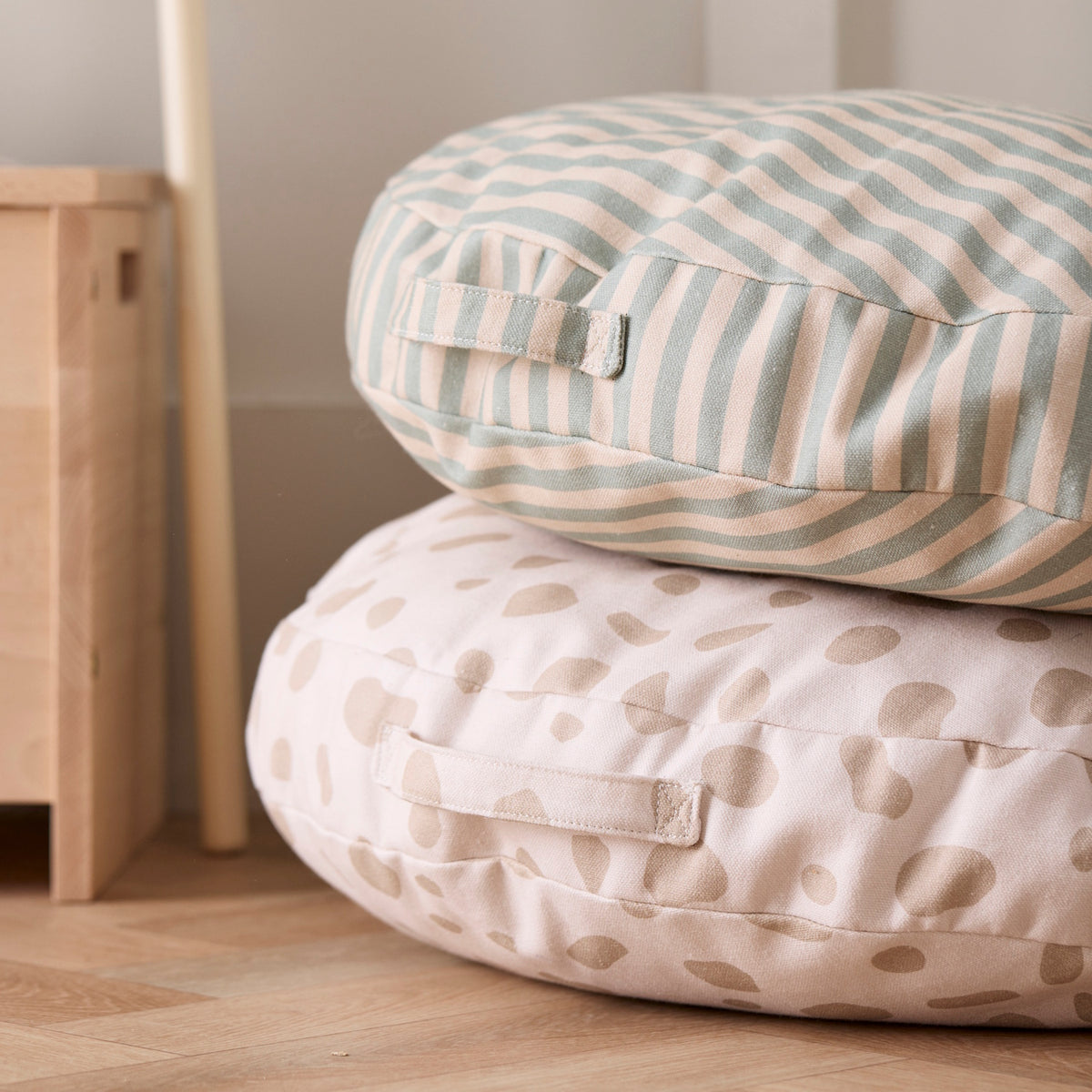 Two round floor cushions stacked together: one with green stripes on top of a spotted cream cushion.