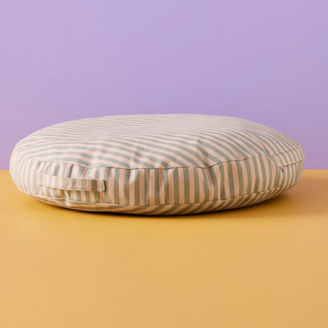 Round sage green and beige striped floor cushion with a fabric handle against a two-tone background.