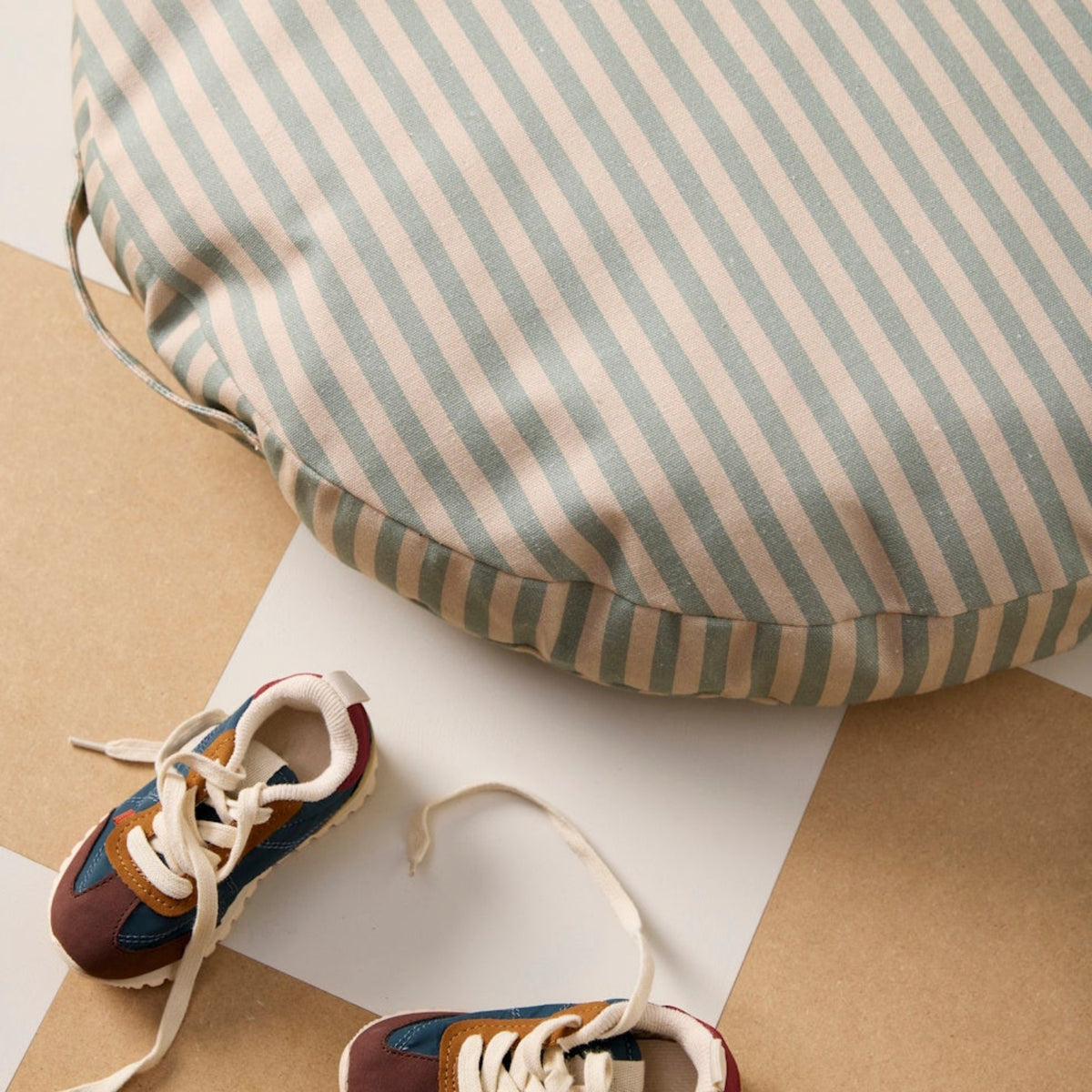 Round green and cream striped floor cushion next to colorful toddler sneakers on a checkered floor.