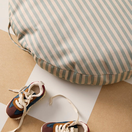 Round green and cream striped floor cushion next to colorful toddler sneakers on a checkered floor.
