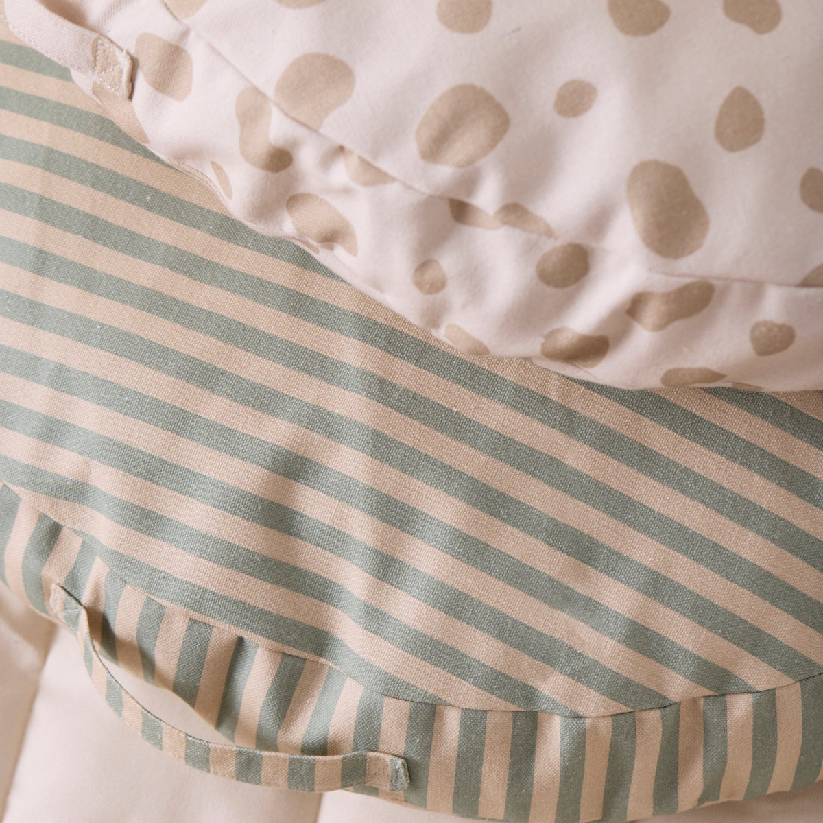 Close-up of a striped beige and green floor cushion stacked beneath a beige polka dot cushion.