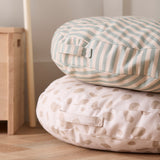 Two stacked round floor cushions: a striped top cushion resting on a beige patterned cushion on a wooden floor.