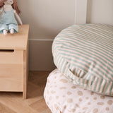 Green and cream striped floor cushion stacked on a spotted cushion next to a wooden chest with a rag doll.