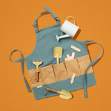 Blue kids gardening apron with beige pockets containing yellow tools, wooden markers, and watering can.