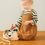 Young child kneeling down while taking a toy gardening tool out of a canvas tote bag.