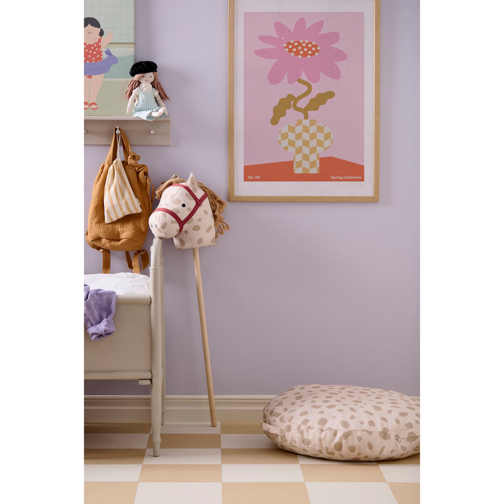 A playful rocking horse head on a stick with a cream base and brown spots. It features a red bridle and yarn mane on a simple wooden stick.