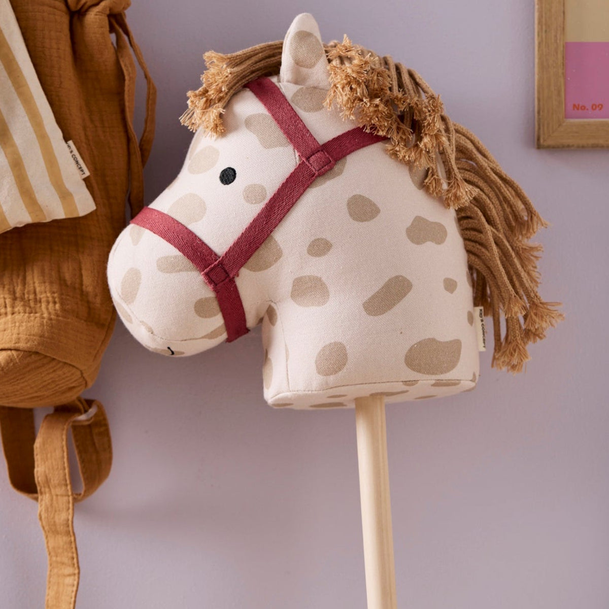 Spotted fabric hobby horse with a red bridle and yarn mane mounted on a wooden stick.