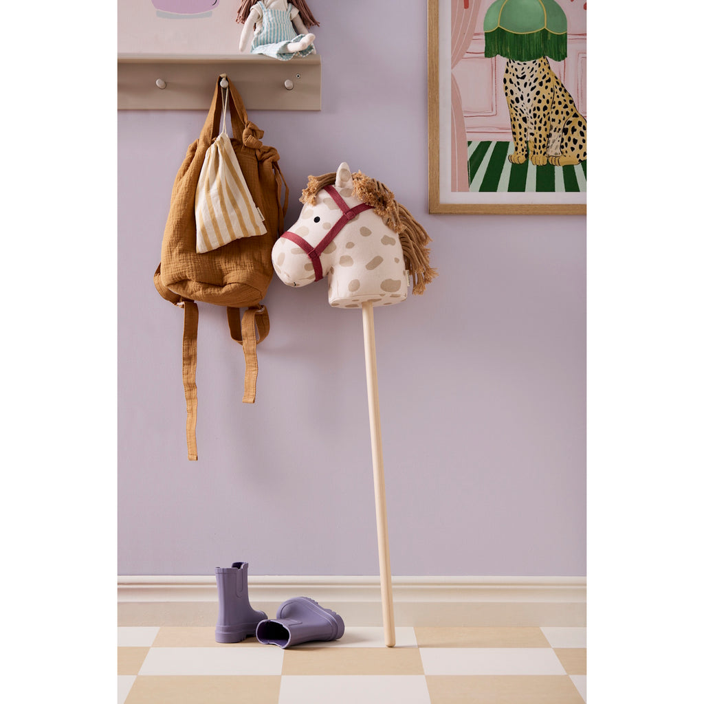 A playful rocking horse head on a stick with a cream base and brown spots. It features a red bridle and yarn mane on a simple wooden stick.