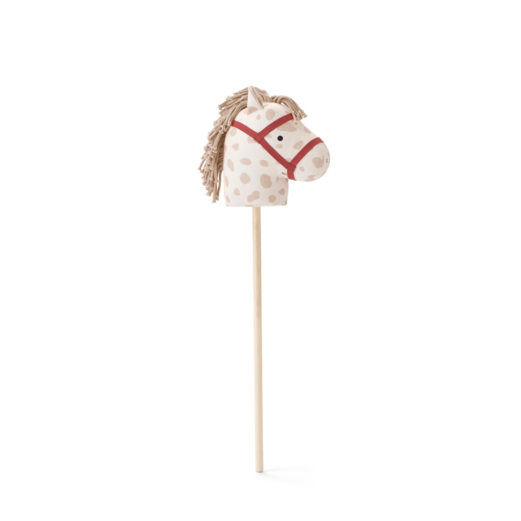 A playful rocking horse head on a stick with a cream base and brown spots. It features a red bridle and yarn mane on a simple wooden stick.