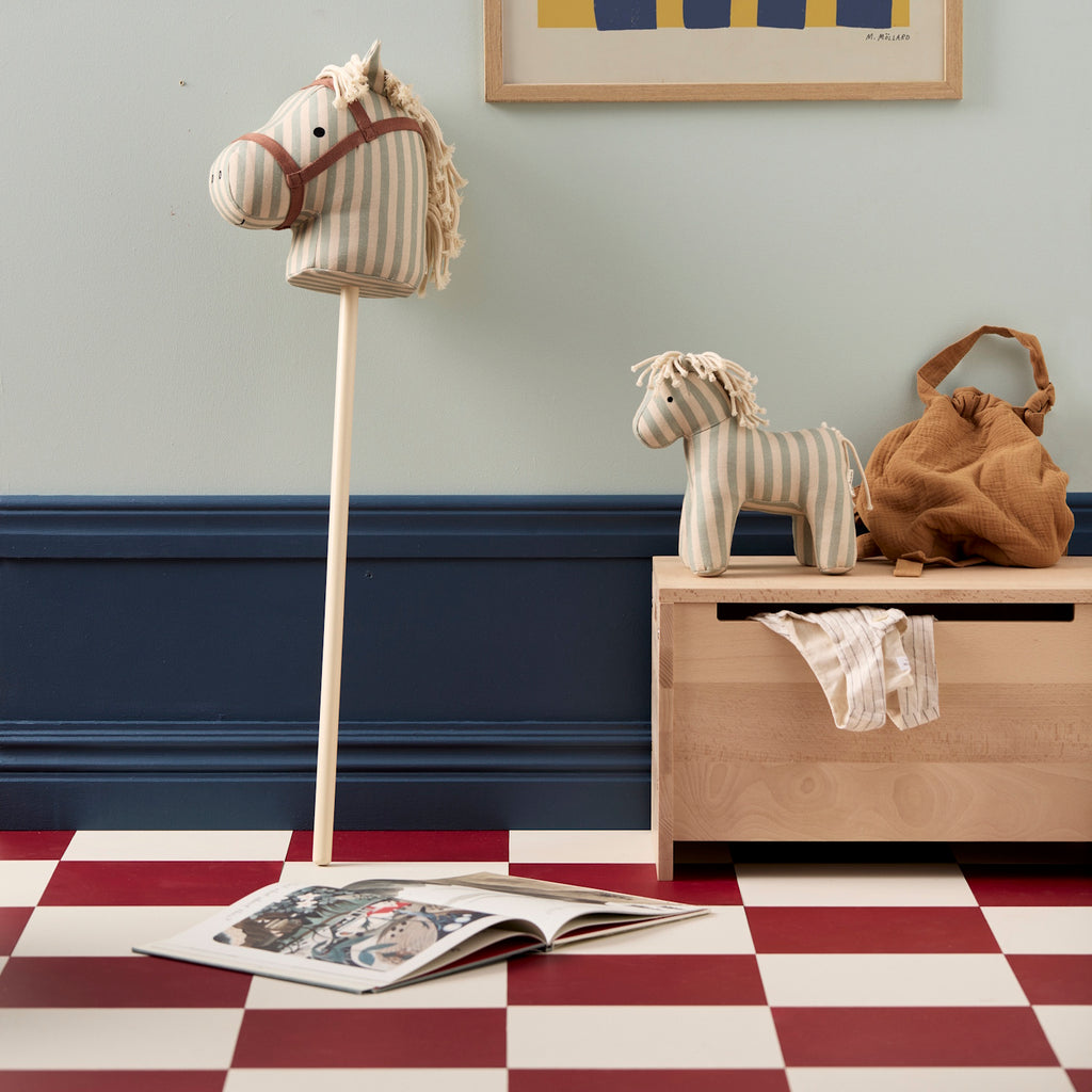 Striped fabric hobby horse toy with a beige and light blue color scheme, featuring a simple face and yarn mane, attached to a wooden stick.