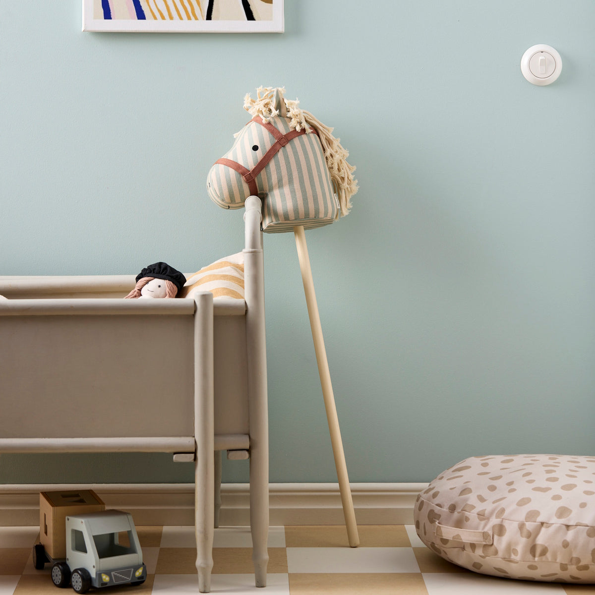 Striped fabric hobby horse leaning against a wooden crib in a decorated playroom.