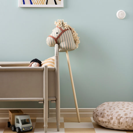 Striped fabric hobby horse leaning against a wooden crib in a decorated playroom.