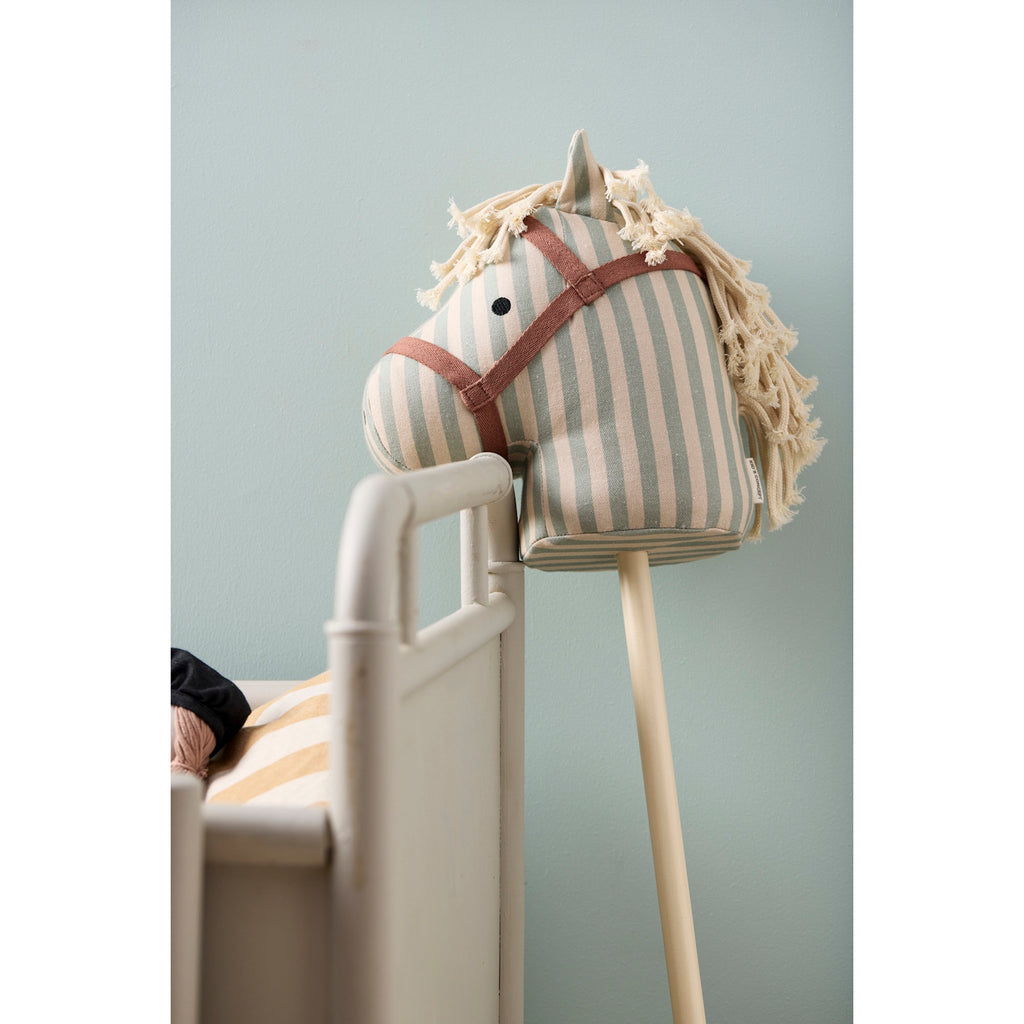 Striped fabric hobby horse toy with a beige and light blue color scheme, featuring a simple face and yarn mane, attached to a wooden stick.