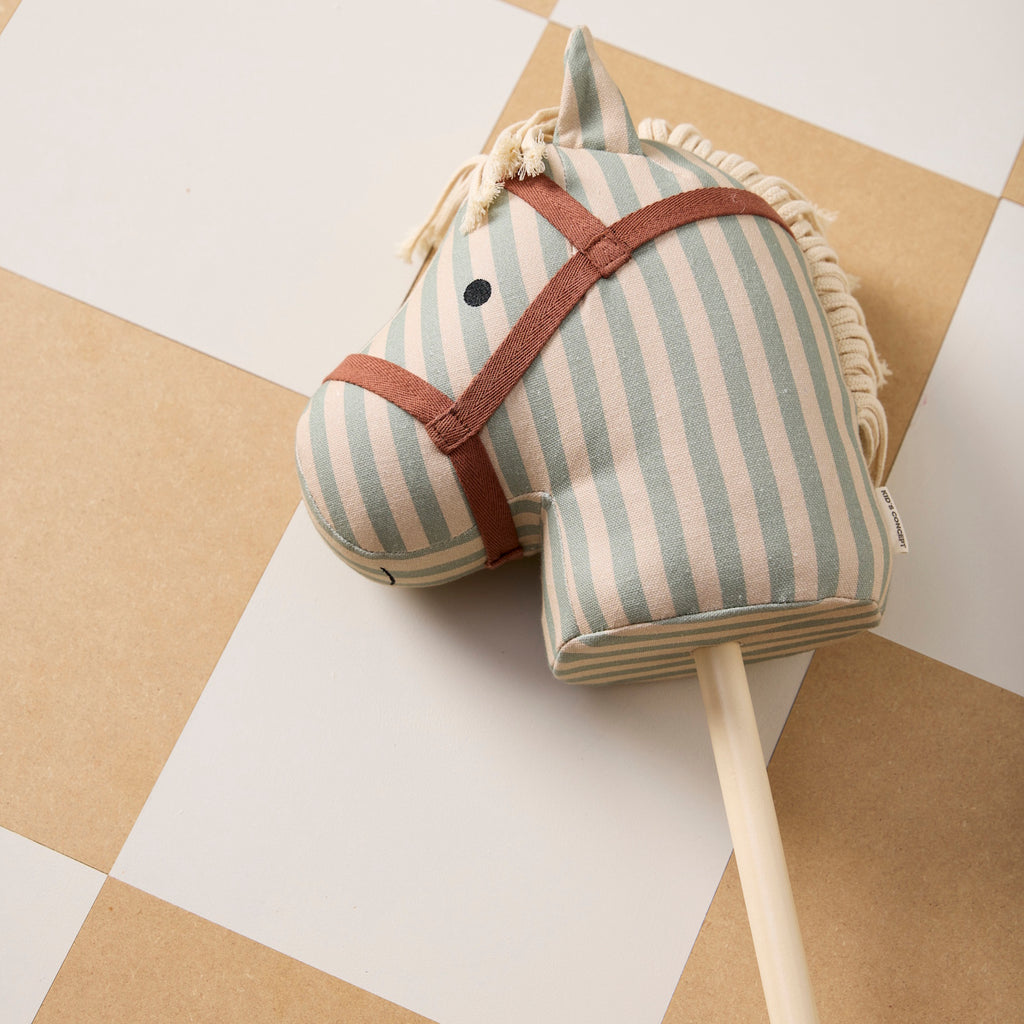 Striped fabric hobby horse toy with a beige and light blue color scheme, featuring a simple face and yarn mane, attached to a wooden stick.