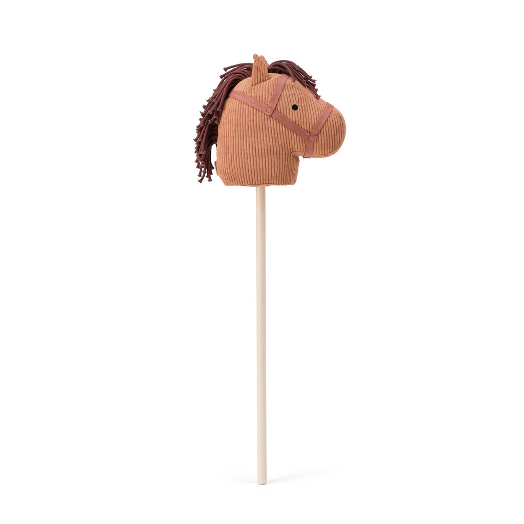 A brown corduroy toy horse head with a maroon mane and harness is mounted on a wooden stick, evoking playful nostalgia and imagination.