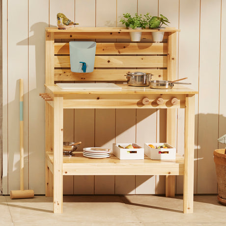 Wooden play mud kitchen arranged with pots, pans, small potted plants, and storage crates against a wooden wall background.