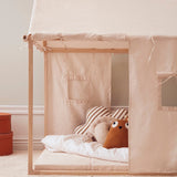 Off-white play house tent set up in a room with soft cushions and an open book on the floor.