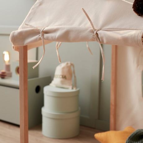 Close-up of off-white play house tent tied to wooden frame with colorful pom-pom garland on top.