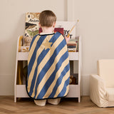 Young child from behind wearing a blue and yellow striped dress-up cape with a gold star badge.