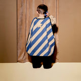 Child from behind wearing a striped dress-up cape, holding a toy walkie-talkie to their ear.