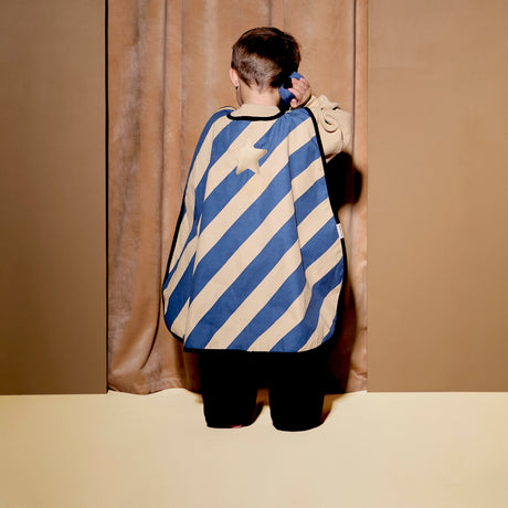Child from behind wearing a striped dress-up cape, holding a toy walkie-talkie to their ear.
