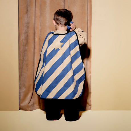 Child seen from behind wearing a striped dress-up cape, holding a toy walkie-talkie to their ear.
