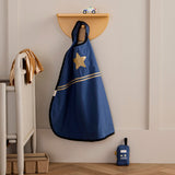 Blue dress-up cape with a gold star badge hanging on a hook next to a toy walkie-talkie.