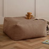 Brown corduroy pouf with a teddy bear and blanket on top, resting on wooden flooring.