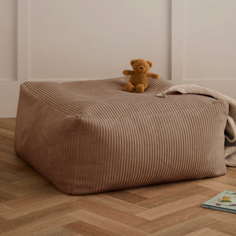 Brown corduroy pouf with a teddy bear and blanket on top, resting on wooden flooring.