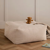 An off-white corduroy floor pouffe with a small teddy bear and blanket resting on top.