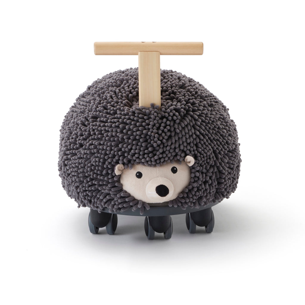 Toy hedgehog with a textured, dark gray surface resembling bristles, mounted on four wheels. It has a wooden handle for riding. Playful and whimsical.