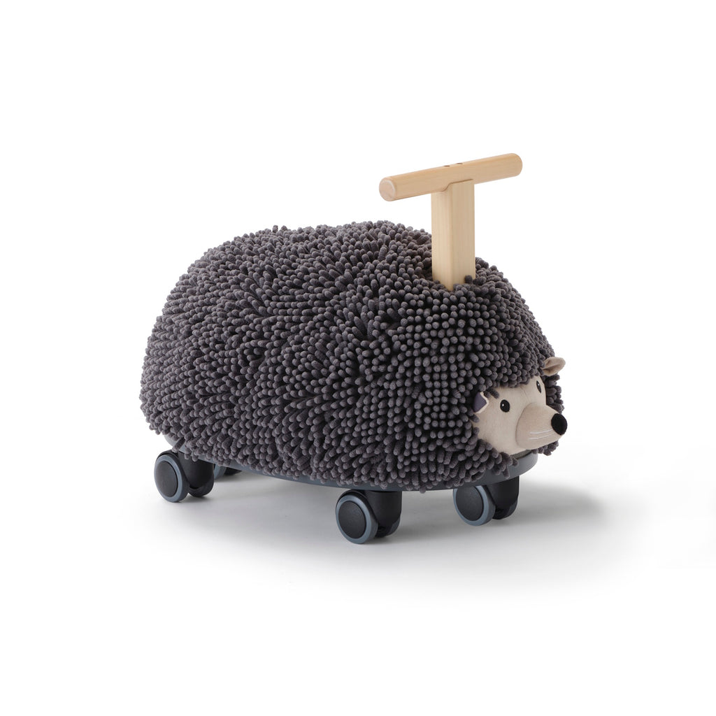 Toy hedgehog with a textured, dark gray surface resembling bristles, mounted on four wheels. It has a wooden handle for riding. Playful and whimsical.